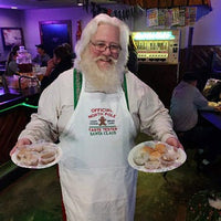 Santa Claus wearing North Pole Taste Tester embroidered white apron. - Life Has Just Begun